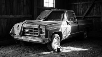 A classic C10 pickup in a barn with a breathable cover pulled partway back